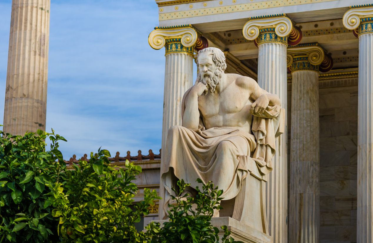 Statue of the greatest Greek philosopher Socrates sitting on a marble chair, background of classical Greek columns.