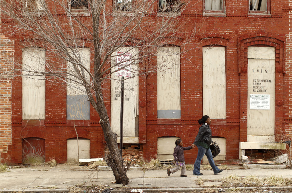 A woman and child walk past a dilapidated building in a run-down neighborhood of Baltimore