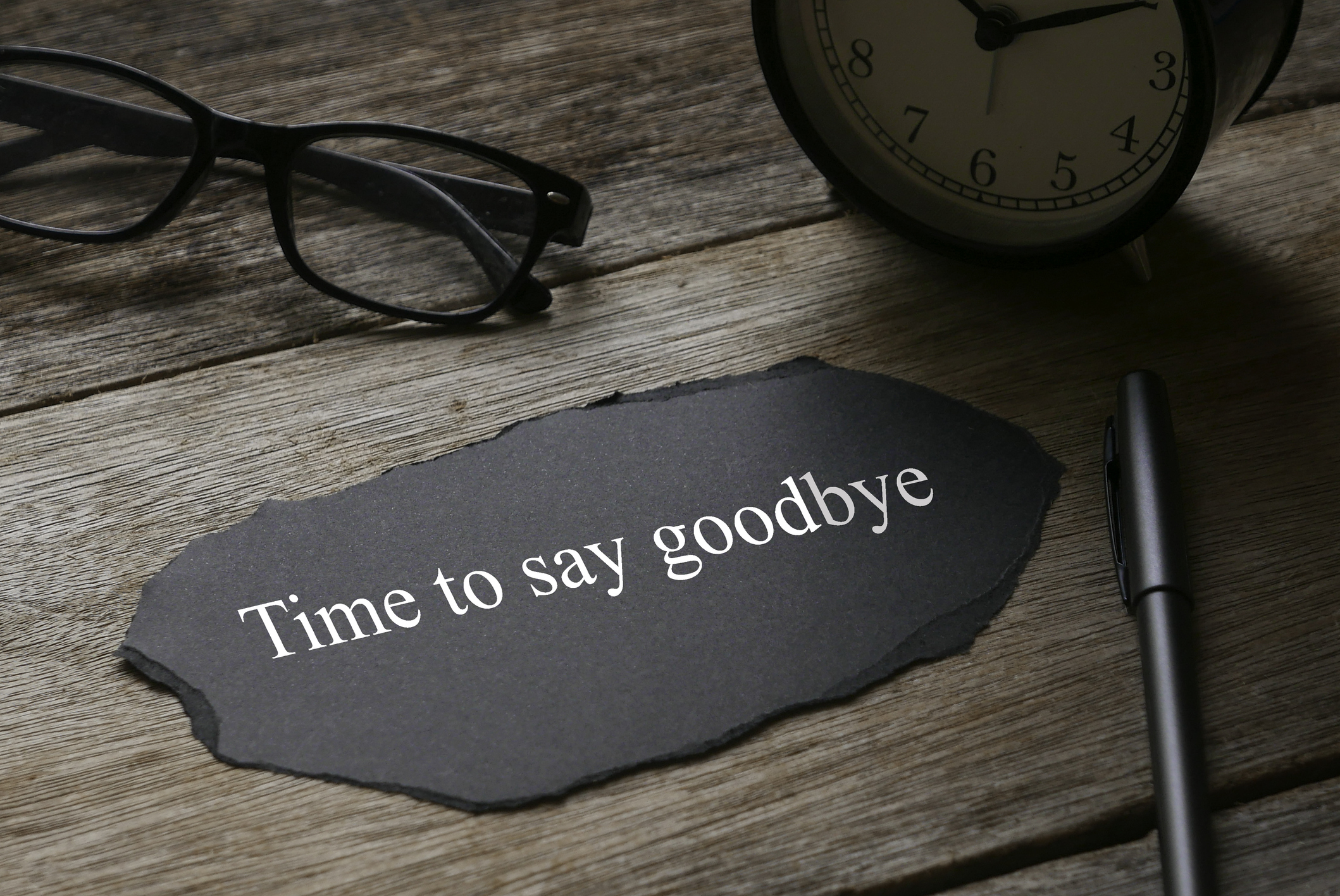 Glasses,clock,pen and a piece of black paper written with Time to say goodbye on wooden background.