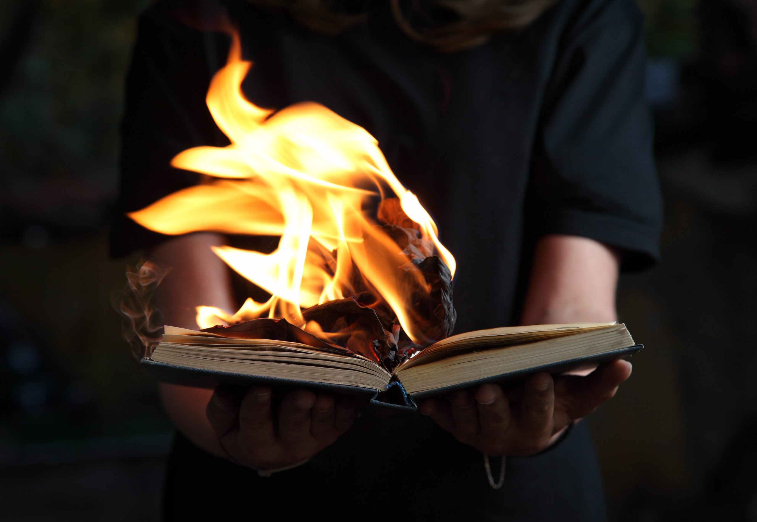 Image of book burning in woman hands in dark forest
