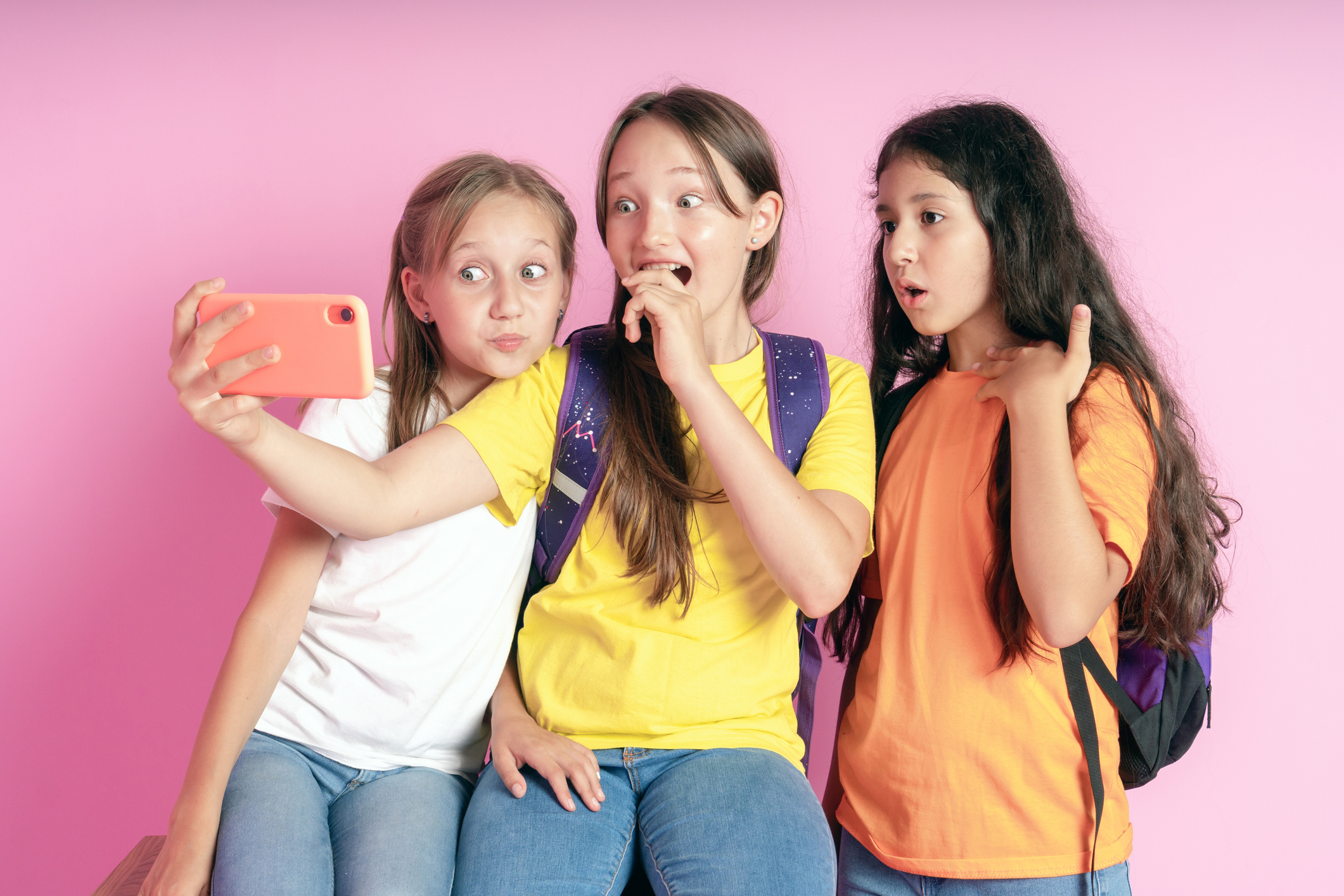 Three teen girls smiling and shoots a video on a pink background.  Selfies. Tiktok blogger.