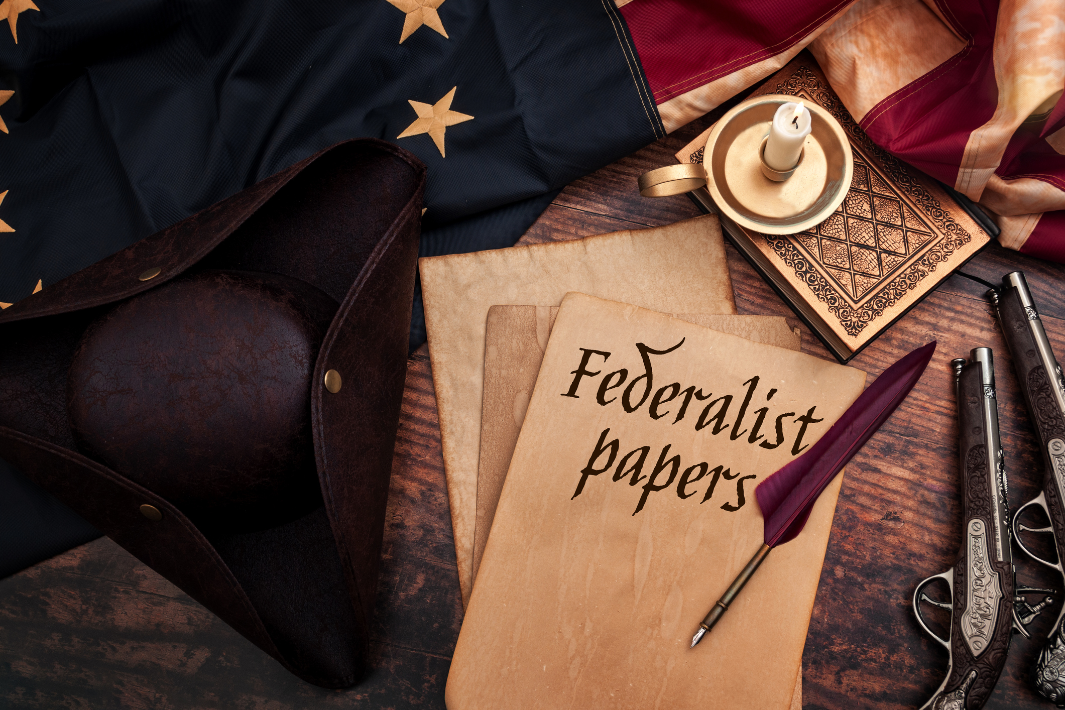 Federalist papers and the birth of the United States of America concept with tricorn hat, candle, feather quill, musket gun, the Betsy Ross American flag and aged paper