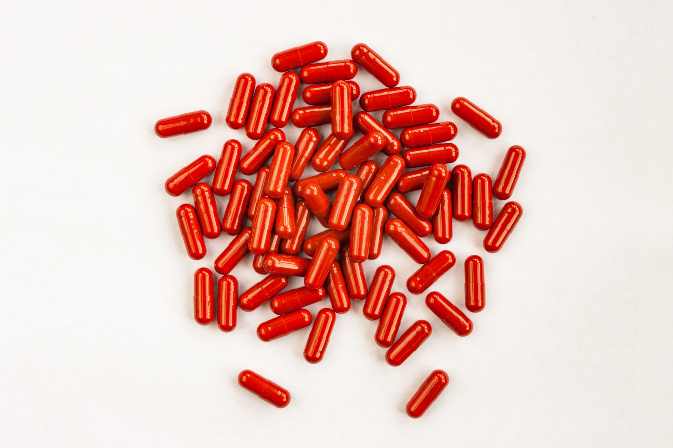 Red capsules pills heap on white background. Medicine pharmacy concept. Close up top view.
