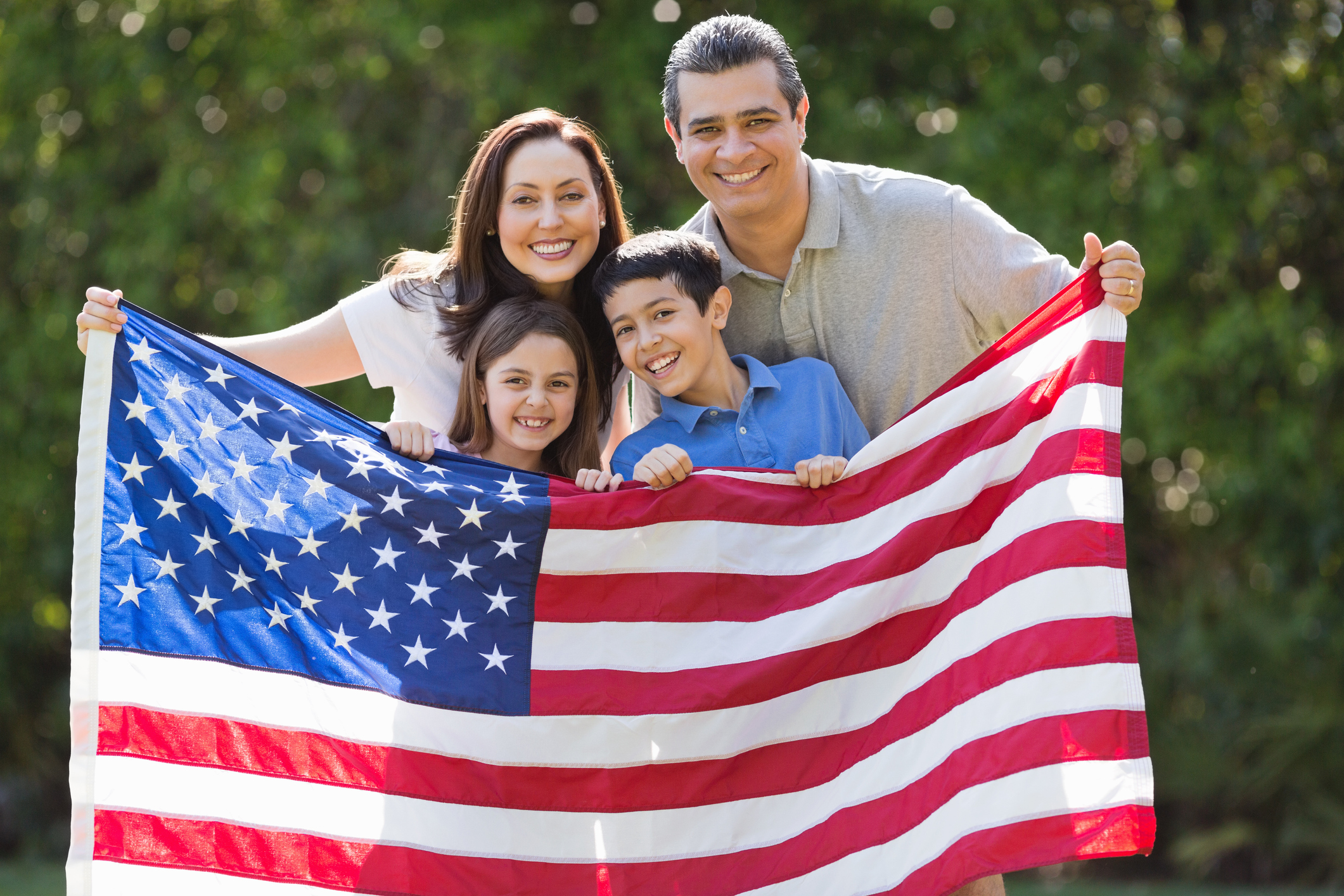 Family Smiling While Holding American Flag At Park