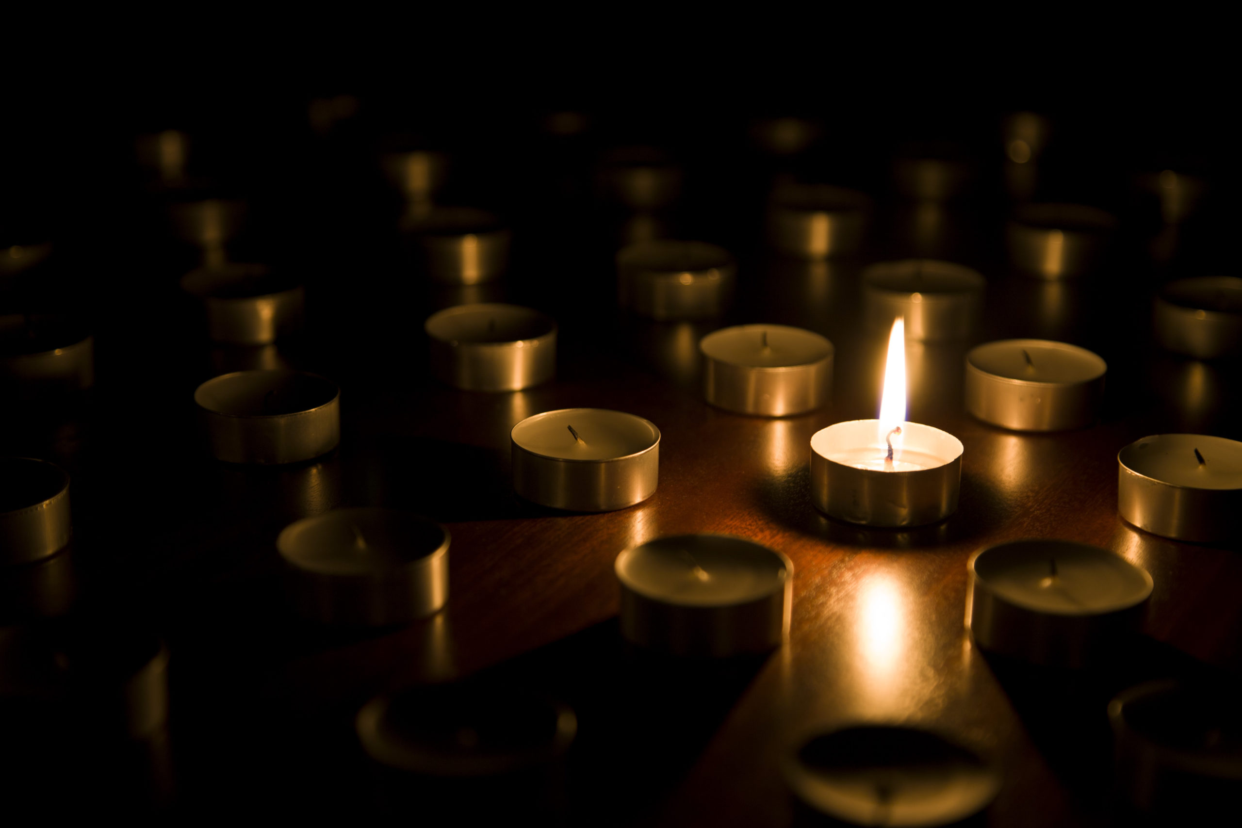 Single lit tealight candle surrounded by unlit tealight candles