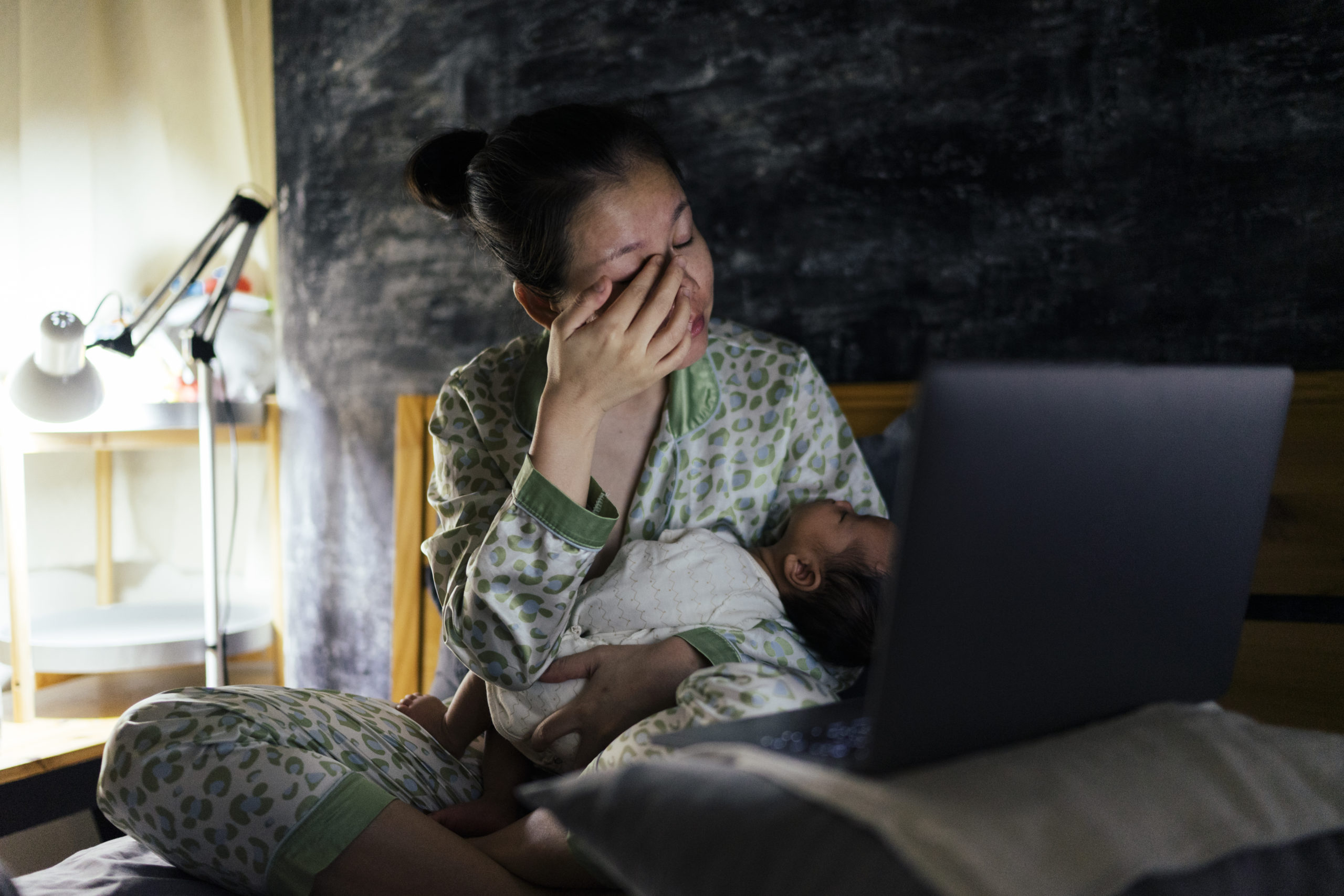 Asian mother wake up late at night for breastfeeding infant and clicking laptop computer on the bed