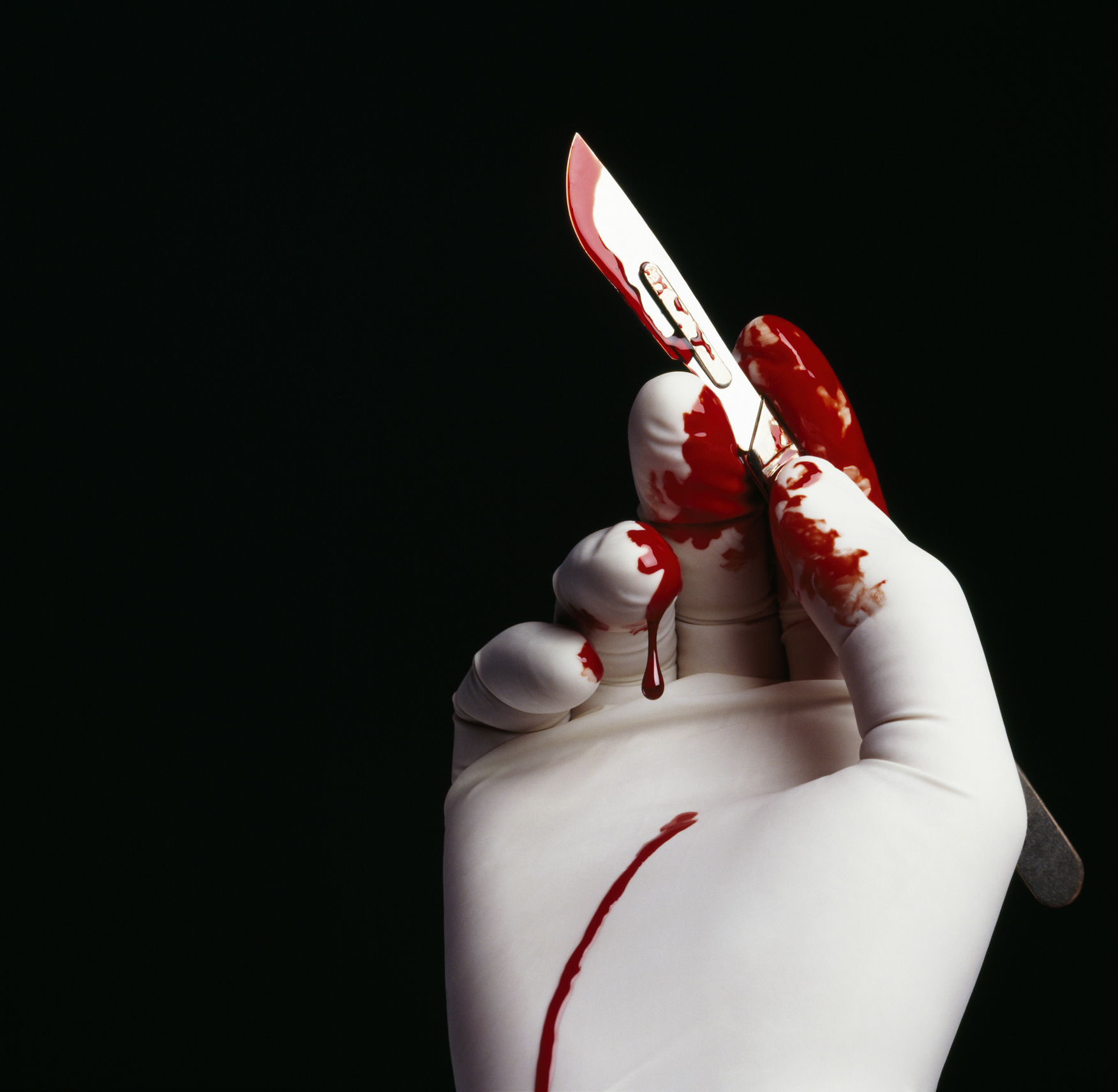 Surgeon holding blood stained scalpel, close-up of hand
