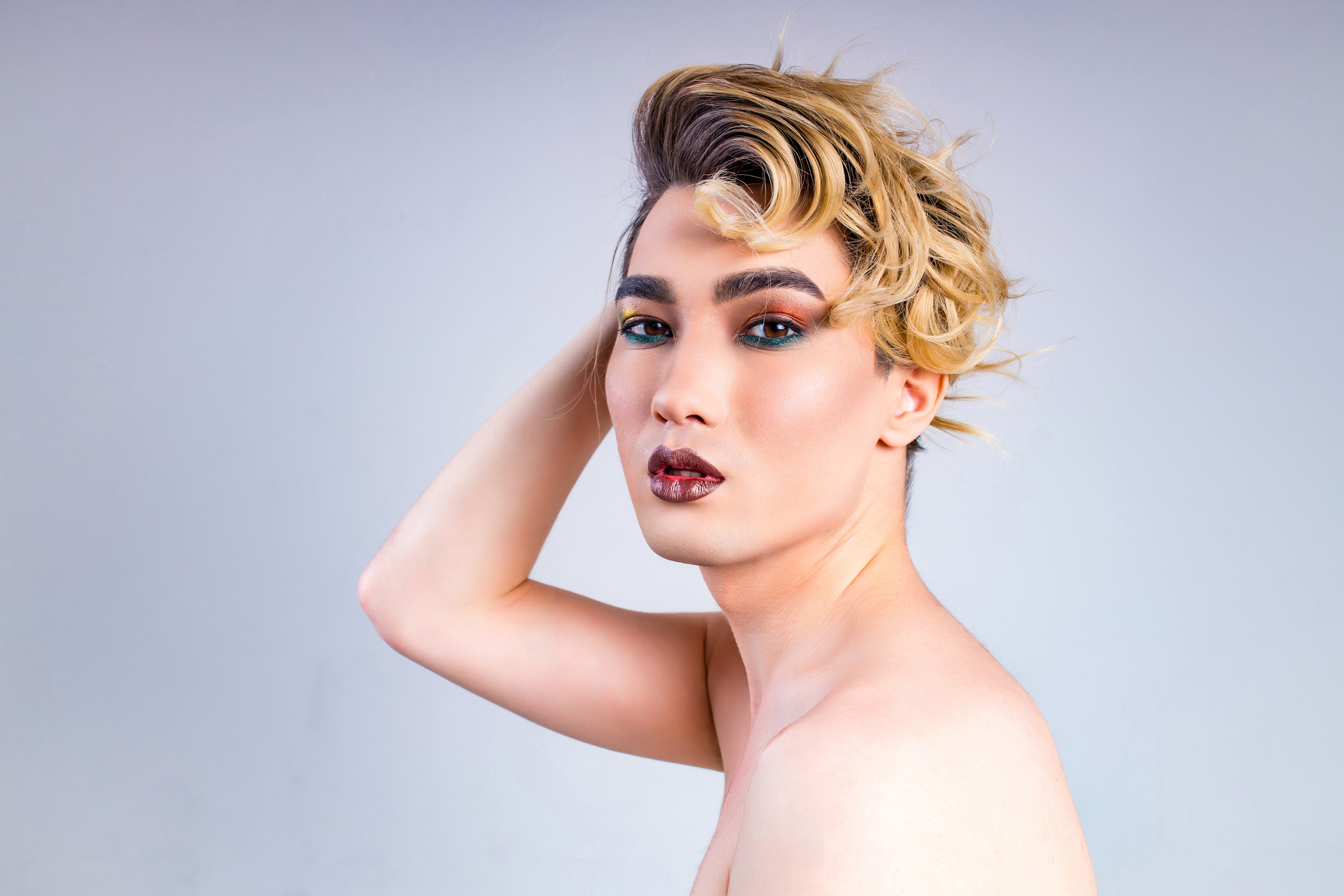 blond man with make up on face posing in studio on white background