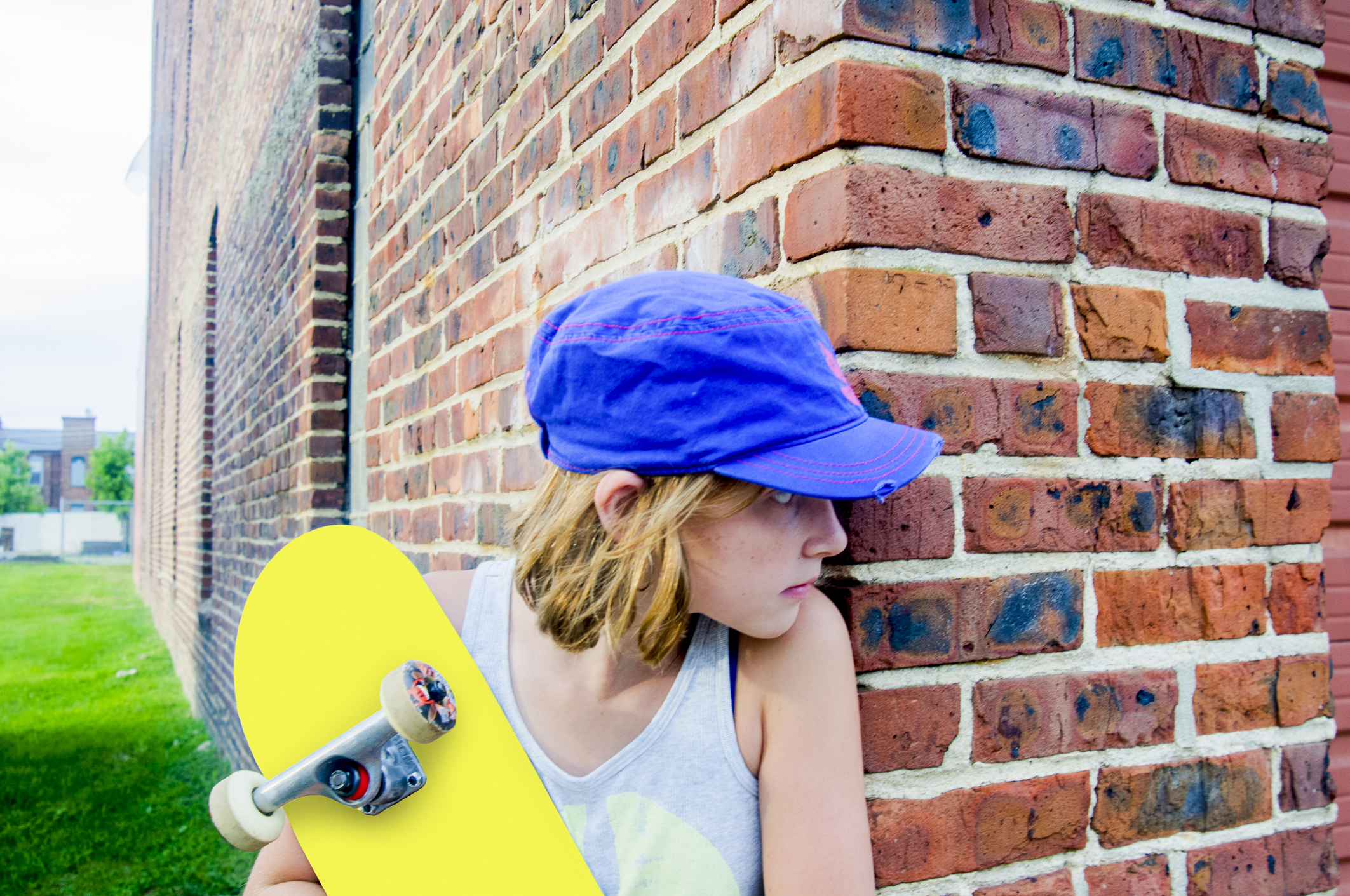 Tomboy skateboarder girl peeking around brick wall corner