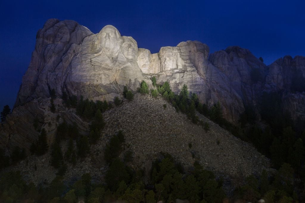 Carved granite busts of George Washington, Thomas Jefferson, Theodore “Teddy” Roosevelt and Abraham Lincoln framed by trees at Mount Rushmore National Monument near Keystone, South Dakota